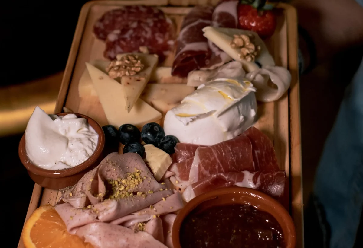 Tabla de embutidos y quesos variados, con jamón, salami, queso, nueces y mermelada, presentada en una bandeja de madera. Ideal para compartir en reuniones o celebraciones.