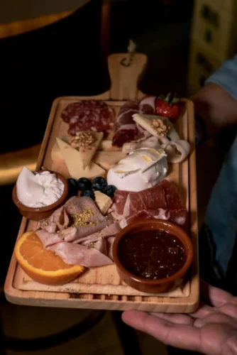 Tabla de embutidos y quesos variados, con jamón, salami, queso, nueces y mermelada, presentada en una bandeja de madera. Ideal para compartir en reuniones o celebraciones.